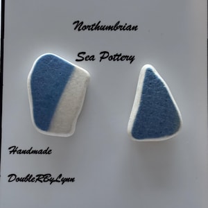 May include: Two pieces of Northumbrian sea pottery. One is an irregular shape with a diagonal blue and white design. The other is a triangle shape with a blue and white design. The words "Northumbrian Sea Pottery" and "Handmade DoubleRByLynn" are written on the white background.