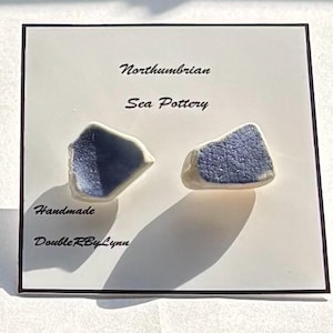 Könnte beinhalten: Ein Paar blaue und weiße Keramikohrringe in Form unregelmäßiger Scherben. Die Ohrringe sind handgefertigt von DoubleRByLynn und sind als Northumbrian Sea Pottery gekennzeichnet.