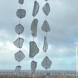 Puede incluir: Un móvil artesanal hecho con piezas de vidrio marino transparente ensartadas en alambre y suspendidas de una rama de madera oscura. El vidrio marino tiene varias formas y tamaños, creando un objeto decorativo único.