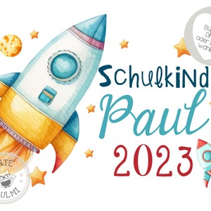 May include: A watercolor illustration of a rocket ship with a blue, yellow, and red color scheme. The rocket is flying through space with stars and planets. The text "Schulkind Paul 2023" is written in blue and red lettering.