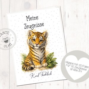 Puede incluir: Una carpeta A4 blanca para boletines escolares con una ilustración de un cachorro de tigre, hojas verdes y el texto Meine Zeugnisse y Karl Fröhlich. Se ve un logo circular con un búho y el texto Tante Ulmi, junto a una etiqueta en forma de corazón.