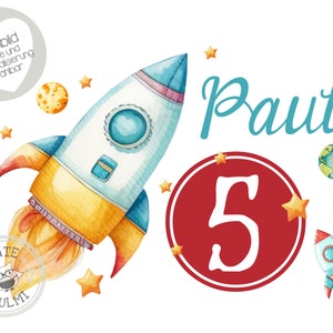 May include: A watercolor illustration of a rocket ship with a yellow and blue design, flying through space with planets and stars. The number 5 is in a red circle, and the name Paul is written in blue.