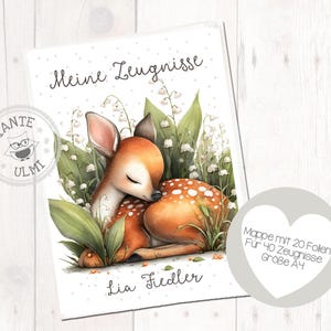 Könnte beinhalten: A4-Ordner mit einer Illustration eines schlafenden Rehs. Das Reh ist braun mit weißen Flecken, umgeben von grünen Blättern und weißen Blumen. Der Text enthält "Meine Zeugnisse" und "Lia Fiedler".