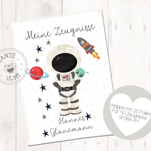 May include: A white card with a blue and white astronaut illustration, a red planet, and stars. The text on the card reads "Meine Zeugnisse Hannes Glanzmann" and "Mappe mit 20 Follen Für 40 Zeugnisse Größe A4".