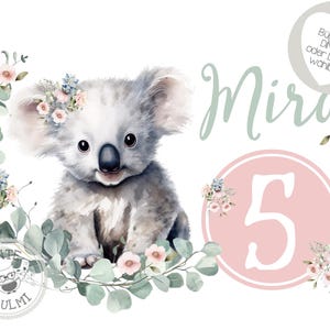 Peut inclure: Un adorable koala portant une couronne de fleurs roses est assis dans une couronne de feuilles vertes et de fleurs roses. Le texte "Mira 5" est écrit dans un cercle sur fond rose.