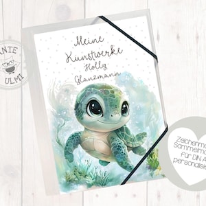 Peut inclure: Un classeur blanc avec une fermeture en ruban noir. Le devant du classeur présente une illustration aquarelle d'une tortue de mer verte aux yeux bleus. Le texte "Meine Kunstwerke Holly Glanzmann" est imprimé sur le classeur.