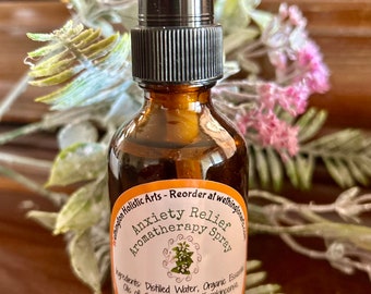May include: Amber glass aromatherapy spray bottle with a black spray nozzle. The label reads "Anxiety Relief Aromatherapy Spray" and lists ingredients. The bottle is surrounded by greenery and flowers.