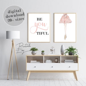 May include: Two printable wall art prints. The first print features the text "BE you TIFUL" in pink script with black text. The second print features a watercolor illustration of a woman wearing a pink dress and heels.