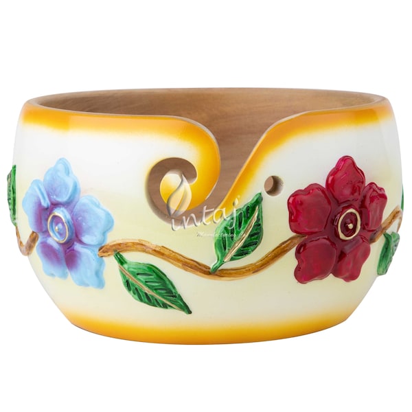 May include: A white wooden yarn bowl with a yellow rim and floral design. The bowl has a carved hole for yarn to pass through. The flowers are painted in shades of red, blue, and green.