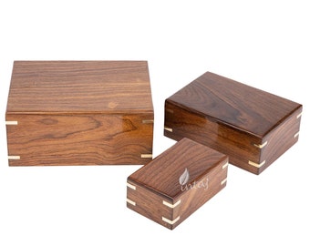 May include: Three wooden boxes of varying sizes with brass accents. The boxes are made of a dark wood with a natural grain pattern. The largest box is in the background, the medium box is in the middle, and the smallest box is in the foreground.