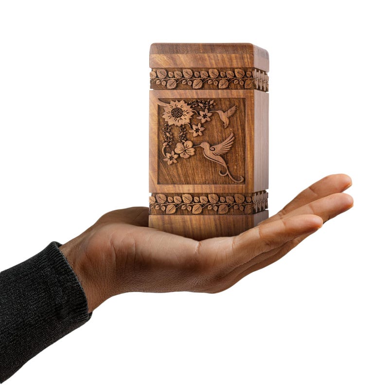 Rosewood hummingbird urn shown next to a wine bottle for scale comparison. Illustrates the physical size of this wooden cremation urn, featuring the clear hummingbird and floral design. Helps visualize the memorial box dimensions.