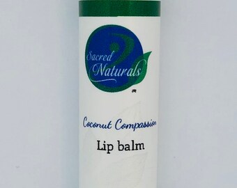 May include: A white tube of lip balm with a green and blue label. The label says "Sacred Naturals" and "Coconut Compassion Lip Balm". It also says "All Natural".
