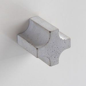Puede incluir: Un pomo de armario de hormigón blanco con forma de estrella de cuatro puntas.