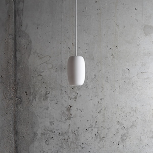 May include: A white pendant light hangs from a wire against a concrete wall.
