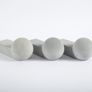 Puede incluir: Tres sujetalibros de hormigón, cada uno con una esfera redondeada en la parte superior de una base rectangular. Los sujetalibros están dispuestos en fila, con las esferas mirando hacia adelante.