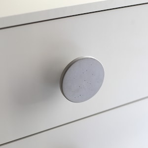 Op de afbeelding: Een witte lade met een ronde, grijze betonnen knop.