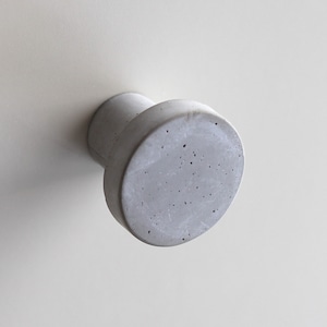 Puede incluir: Un pomo de hormigón gris con una base redonda y un vástago cilíndrico. El pomo tiene una superficie rugosa y texturizada.