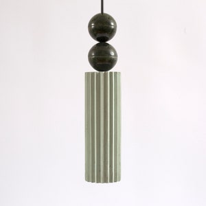 May include: A green, fluted, cylindrical pendant light fixture with two dark green spheres hanging from it.