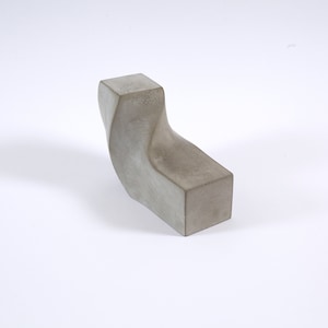 Op de afbeelding: Een grijs betonnen beeldhouwwerk met een unieke, gedraaide vorm. Het beeldhouwwerk is abstract en modern van stijl.