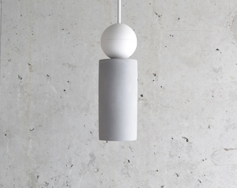 May include: A gray concrete pendant light with a white sphere on top. The light is hanging from a white ceiling.