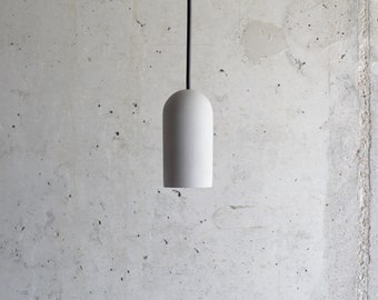 May include: A white concrete pendant light fixture with a black cord hanging from a ceiling.