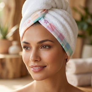 Puede incluir: Una toalla para el cabello blanca con un borde de cuadros en tonos pastel y peque&ntilde;os motivos de flores rosas y azules. La toalla est&aacute; retorcida y asegurada en la parte delantera, mostrando una textura suave y afelpada. El texto Style - 10 aparece abajo.