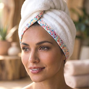Puede incluir: Una toalla de pelo blanca y afelpada con un borde de estampado floral colorido en tonos rosa, naranja y verde. La toalla est&aacute; enrollada en forma de turbante alrededor de la cabeza, con el texto Main Style impreso en la parte inferior.
