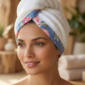 Puede incluir: Una toalla de pelo blanca de felpa con un borde azul con un estampado floral rosa y verde. La toalla est&aacute; retorcida y asegurada en la parte delantera, mostrando una textura suave y absorbente. El texto "Style - 5" aparece en la parte inferior.