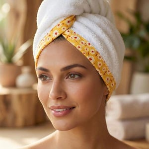 Puede incluir: Una toalla para el cabello blanca con un borde amarillo que presenta un patr&oacute;n repetitivo de margaritas blancas. La toalla est&aacute; asegurada en un estilo de turbante retorcido alrededor de la cabeza. El texto "Style - 2" aparece en negro.