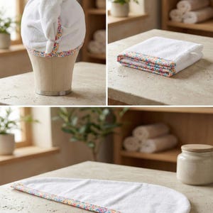 Puede incluir: Una toalla blanca para el cabello con un borde floral colorido. El conjunto incluye una toalla doblada, una toalla extendida y una toalla colocada sobre una cabeza de maniqu&iacute;. La tela es suave y absorbente con un patr&oacute;n multicolor vibrante.