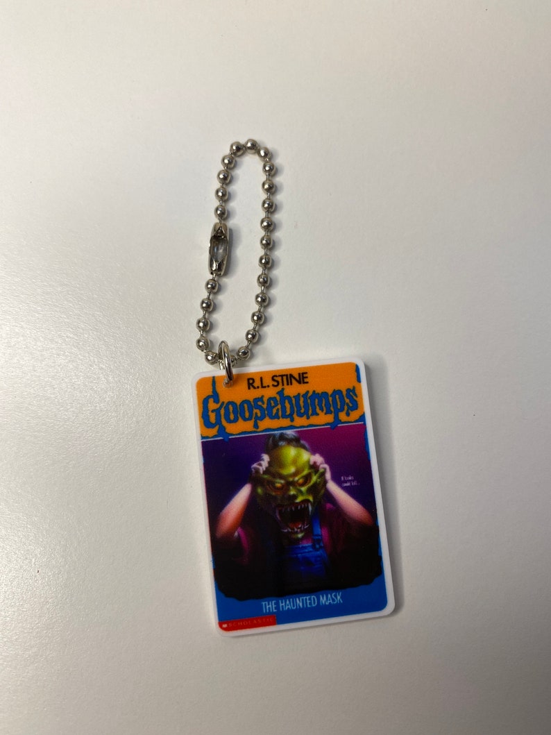 Puede incluir: Un llavero de Goosebumps con una portada de libro que muestra un monstruo verde con una m&aacute;scara. El t&iacute;tulo del libro es "The Haunted Mask" de R.L. Stine.