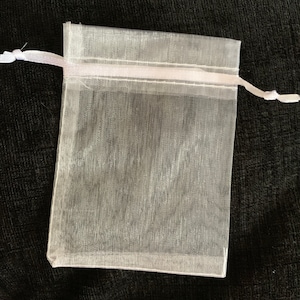 Puede incluir: Una bolsa de regalo de organza blanca transparente con un cord&oacute;n de sat&eacute;n blanco.