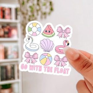 May include: A sticker sheet featuring summer-themed illustrations. Designs include a rainbow-colored life preserver, a watermelon slice, pink bows, a unicorn float, a seashell, a flamingo float, a beach ball, and the text "GO WITH THE FLOAT."