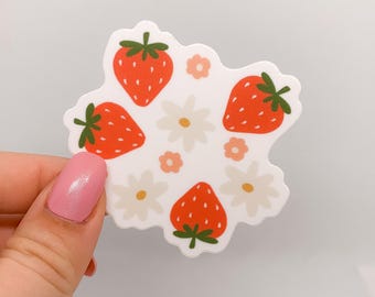 May include: A white sticker with a red and green strawberry and white flower design.