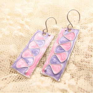 May include: A pair of silver earrings with pink and purple enamel. The earrings are rectangular in shape and have a swirling pattern.