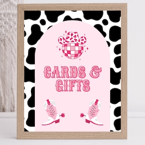 Puede incluir: Un cartel rosa y blanco con fondo de estampado de vaca. El cartel dice "Cards & Gifts" y tiene un sombrero de vaquero rosa y botas a cada lado.