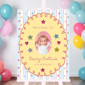 May include: A birthday party welcome sign with a photo of a young girl wearing a crown, surrounded by balloons in shades of pink, blue, and yellow. The sign reads "Welcome to Nancy Collin's 5th Birthday" in a decorative font, with star and heart accents.