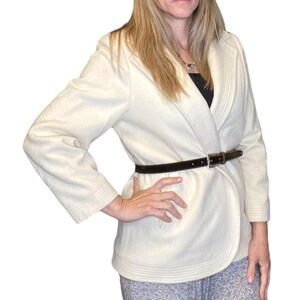 Peut inclure: Un blazer blanc cassé doté de manches longues avec des poignets côtelés, un col châle à texture côtelée verticale et une fine ceinture en cuir marron foncé avec une boucle en métal argenté serrée à la taille sur un haut noir.