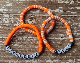 May include: Two orange and white beaded bracelets with the words "Tennessee" and "VOLS" spelled out in white letters.