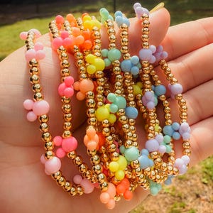 May include: A set of colorful beaded bracelets with gold accents and Mickey Mouse shaped charms. The bracelets are layered on top of each other and are arranged in a rainbow pattern.