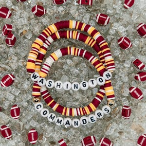 May include: Red, white, and gold beaded bracelets with the words "WASHINGTON COMMANDERS" spelled out in white letters.