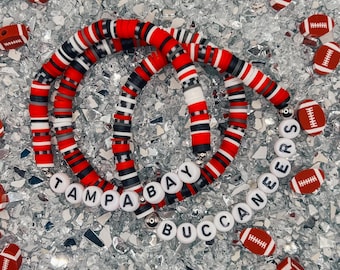 Puede incluir: Tres pulseras de cuentas rojas, blancas y negras con las palabras "Tampa Bay Buccaneers" escritas en letras blancas.