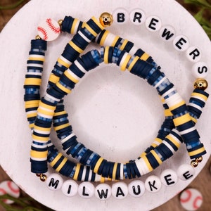 May include: A multi-strand bracelet with blue, white, and yellow beads. The bracelet has a baseball charm and letter beads that spell "Brewers Milwaukee".