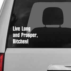 Puede incluir: Adhesivo de vinilo blanco aplicado a una ventana de coche. El adhesivo presenta la frase "Live Long and Prosper, Bitches!" en una fuente en negrita, sin serifa. La imagen muestra la parte trasera de un vehículo con una luz trasera roja.