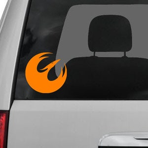 以下が含まれることがあります： グレーの車の窓に貼られた明るいオレンジ色の反乱同盟軍のシンボルステッカー