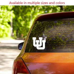 May include: A white vinyl decal of the University of Wyoming's logo, the letter "W" in a blocky font, is displayed on the back window of a red car.