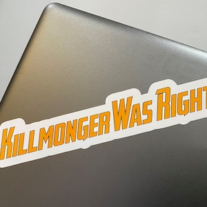 Könnte beinhalten: Ein weißer Aufkleber mit schwarzem Umriss auf einem silbernen Laptop. Der Aufkleber sagt "KILLMONGER WAS RIGHT" in orangefarbenen Buchstaben.