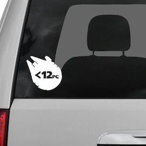 Op de afbeelding: Een witte auto-raamsticker met een silhouet van het Millennium Falcon-ruimteschip uit Star Wars. De sticker heeft de tekst "<12pc" in het ruimteschip.
