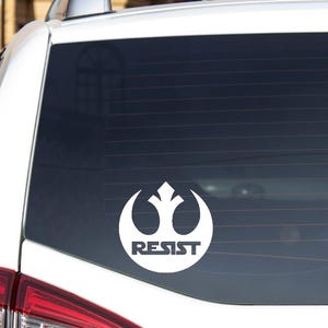 May include: White car window sticker with a white rebel alliance symbol and the word "RESIST" underneath.