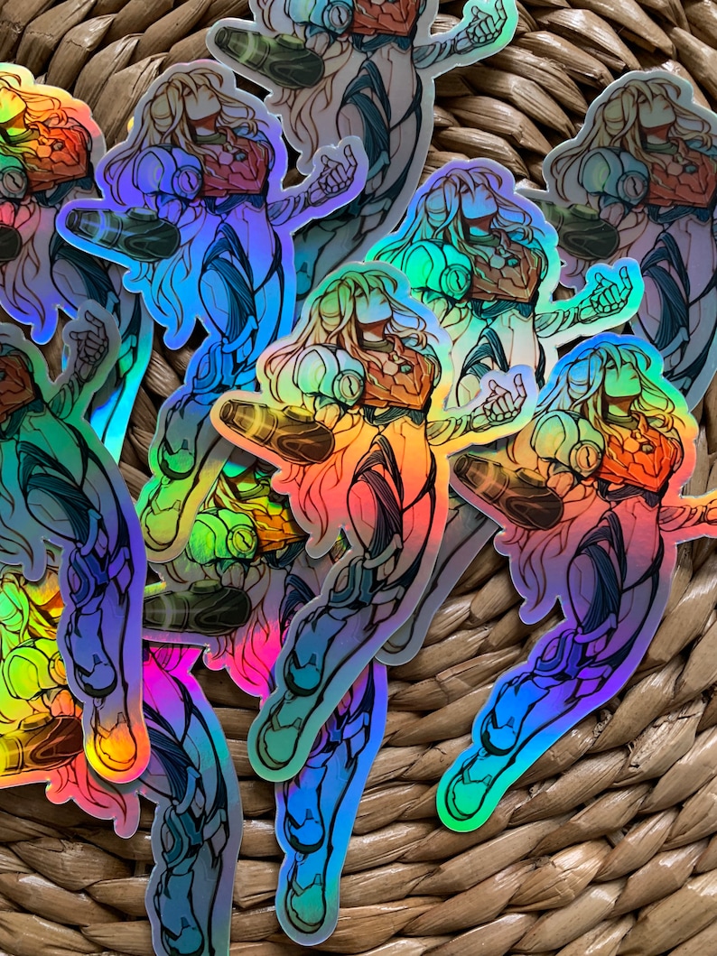 May include: A set of iridescent holographic stickers featuring a female character in a futuristic suit. The stickers are arranged in a pile on a woven wicker surface.